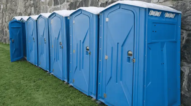 Row of blue portable toilets lined up on grass against a stone wall for event sanitation in Albany, NY