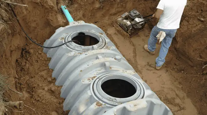 Septic tank installation showing a technician compacting soil around a new poly septic tank in an excavation pit in Albany, NY
